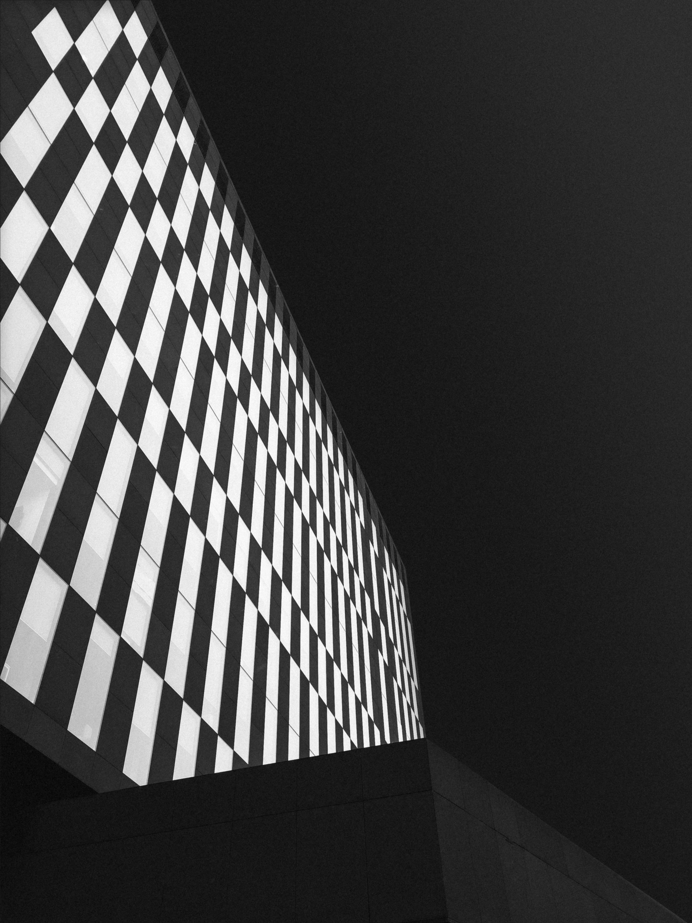 A chequered concrete facade dissolving into shadow
