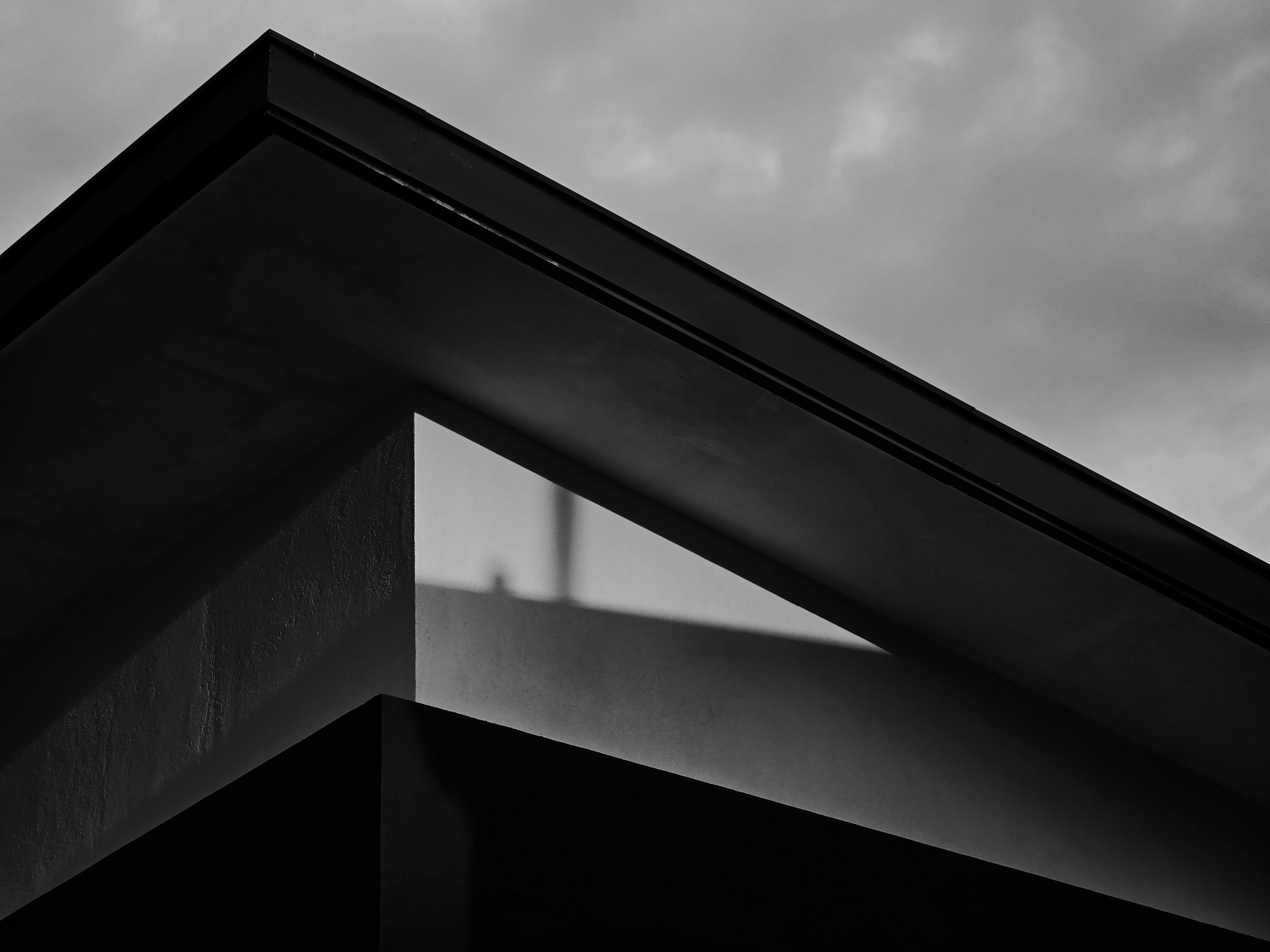 The dark angular eave of a concrete building against a bank of cloud